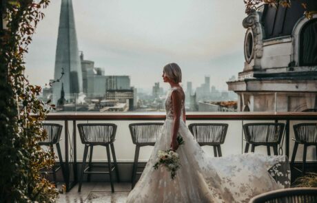 A bride with a white lace dress, walks along the Wagtail terrace overlooking London Bridge and the Shard with her bouquet with with anemones in hand